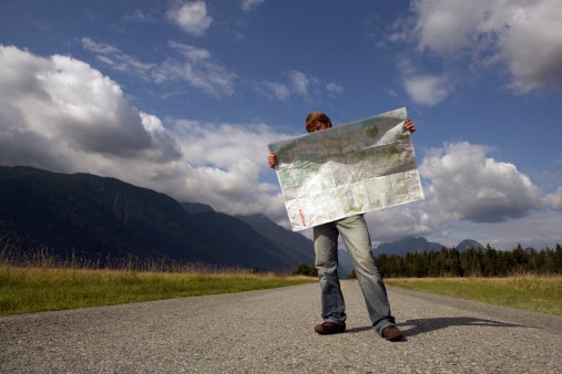 Image of man standing on rural road reading road map